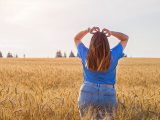 a girl in a field with golden wheat looks at the sun and enjoys nature and freedom