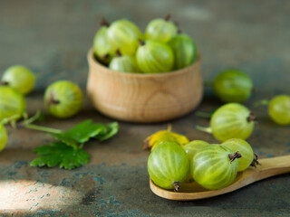 Ripe green gooseberries in a wooden bowl and spoon on an old iron background. Vegetarian food.