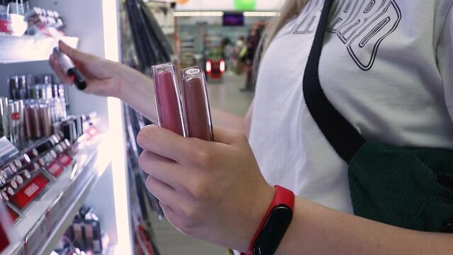 woman shopping for beauty products in cosmetics store, taking lipstick tester from shelf