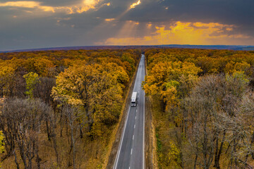 Cargo delivery. white truck driving on an asphalt road through the autumn forest. cargo transportation. Sunset. Drone photo  aerial view