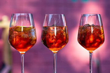 Three glasses of Aperol Spritz close up with pink background