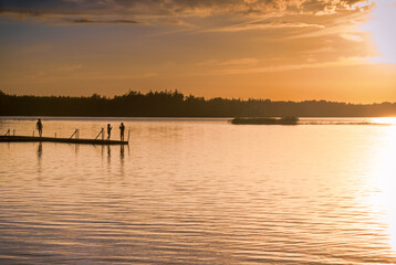 Fototapeta na wymiar A quiet lake in the south of Sweden overlooking a wooden jetty with people in the sunset