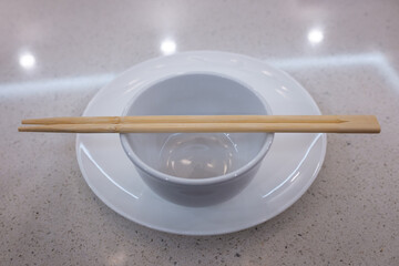 Wood chopsticks and white empty bowl on a white plate in a white table