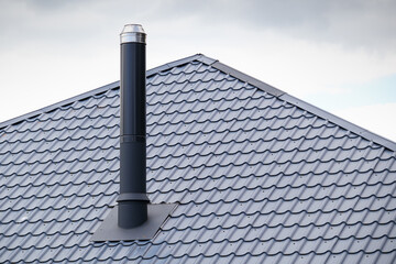 Metal tile roof and metal chimney. Chimney on the roof of the house