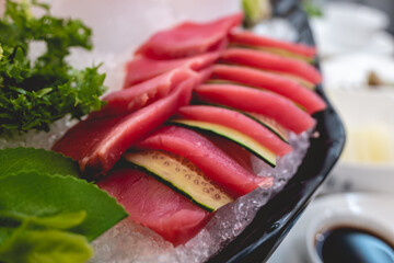 Beautiful and delicious shell arrangement of sashimi slices of sushi on ice with tuna and cucumber and green decoration in a table with food