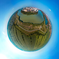 the western outskirts of the city of Krasnodar with multi-storey buildings, washed by the wide river Kuban - a small planet aerial panorama on a sunny day - obrazy, fototapety, plakaty