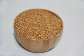 Mustard seed in a wooden bowl, isolated on white background, top view with selective focus.