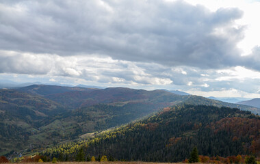Fototapeta na wymiar Autumn mountain landscape with hills covered picturesque and colorful forest under low clouds. Carpathian Mountains, Ukraine