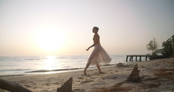 Wide shot portrait of confident woman in tutu performing arabesque and dancing in sunshine on sandy beach. Talented graceful Caucasian ballerina in sunrays outdoors. Slow motion. Cinema 4k ProRes HQ