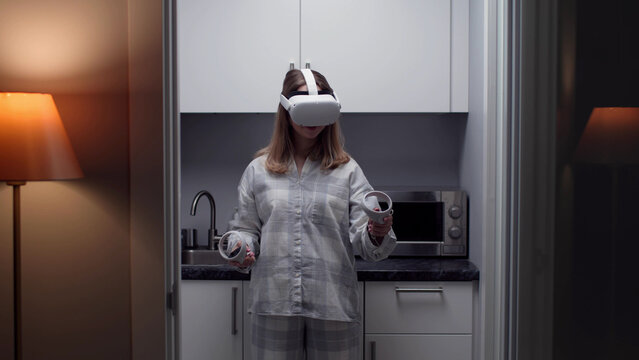 Young woman wearing pajamas play in vr headset at home