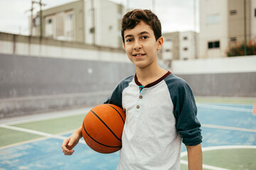 Portrait of 12 year old boy with basketball. Teenager training basketball outdoors.