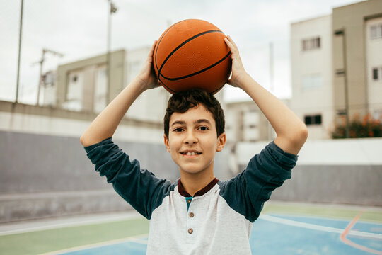 Portrait of 12 year old boy with basketball. Teenager training basketball outdoors.