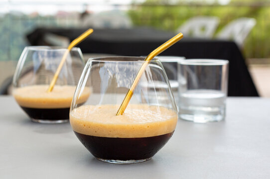 Caffe shakerato with a metal straw. Italian cold drink prepared using espresso and ice cubes in a cocktail shaker. Italian summer coffee beverage.