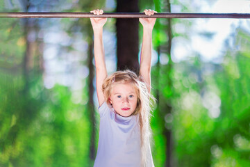 Fototapeta premium Little girl hanging on a horizontal bar in the forest