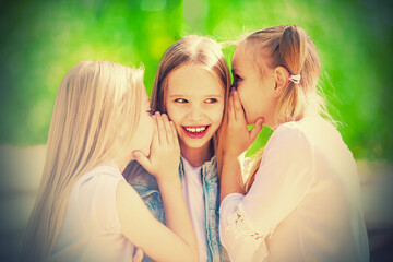 Three cheerful young girls are whispering for a walk in the park