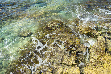 Stone reef covered with green sea water. The coastal cliff is washed by the waves. Texture of stone and water.