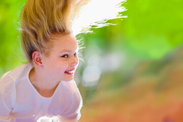 Cheerful young girl with long blond hair hangs upside down outdoors in the park. Sunny summer day