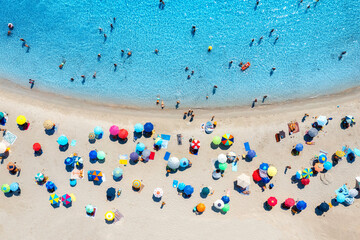 Aerial view of colorful umbrellas on sandy beach, people in blue sea at sunset in summer. Tuerredda Beach, Sardinia, Italy. Tropical landscape with turquoise water. Travel and vacation. Top view	