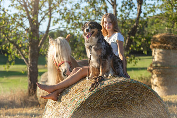 Country kids: A teenage girl sitting on a bale of straw with her australian shepherd dog and her...