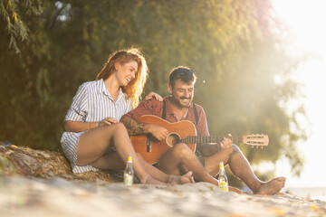 couple sitting on the beach and playing guitar