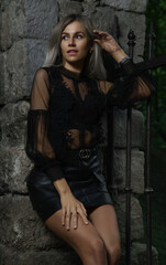 Blonde woman in leather black skirt and transparent shirt standing in ancient castle