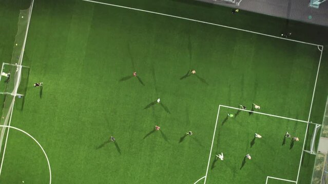 Aerial view of a bright green soccer field during an evening training session. Players are football players moving around the field. Team training, sports exercises