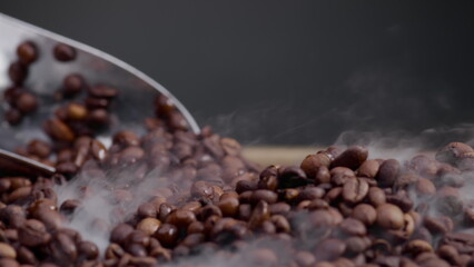 Ladle scooping up coffee beans close up. Light smoke coming over fresh grains.