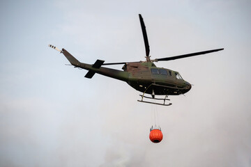 Fototapeta na wymiar Wildfire firefighting in forest with helicopter carrying a water bucket