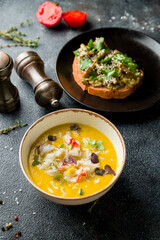 pumpkin cream soup with crab on the bowl on dark table with brushetta with avocado and mushrooms at side, vertical view