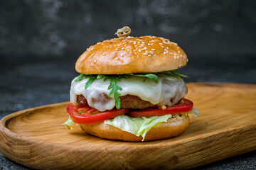 Burger with meat patty, cheese, fresh vegetables and aragula on the board on dark stone table