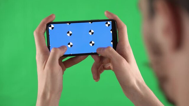 Man with beard holds phone layout horizontally in hand and presses with finger and scales image. Mock-up of Caucasian man with markers for editing on blue display against background chromakey.