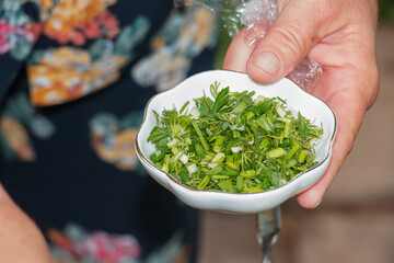 Finely chopped dill, parsley and green onions are held in a saucer by a woman's hand.