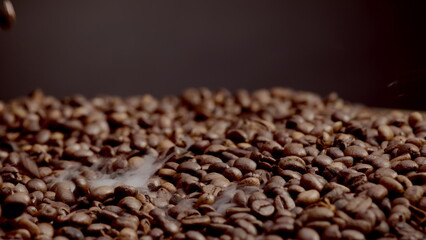 Roasted coffee beans steaming close up. Aromatic grains falling down on heap.