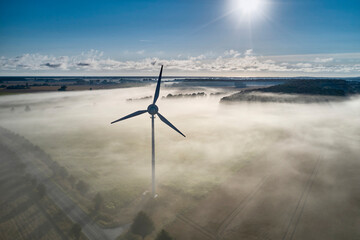 onshore wind turbine standing in fog in the morning sun