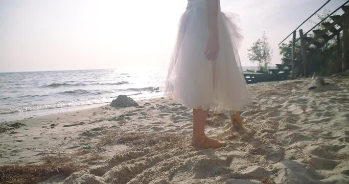 Side view unrecognizable ballerina making steps in slow motion walking in sunbeam on sandy beach. Slim graceful confident Caucasian ballerina strolling outdoors. Cinema 4k ProRes HQ