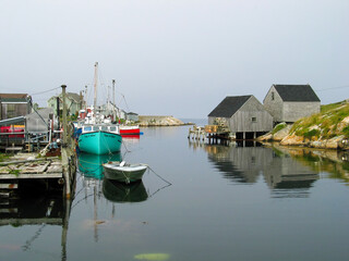 Fototapeta na wymiar Boats are seen docked in a harbour in the small fishing village of Peggy's Cove, Nova Scotia on an overcast and gloomy day, with their reflections resting in the calm water.