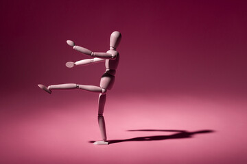 wooden mannequin stands on one leg on a pink background with copy space