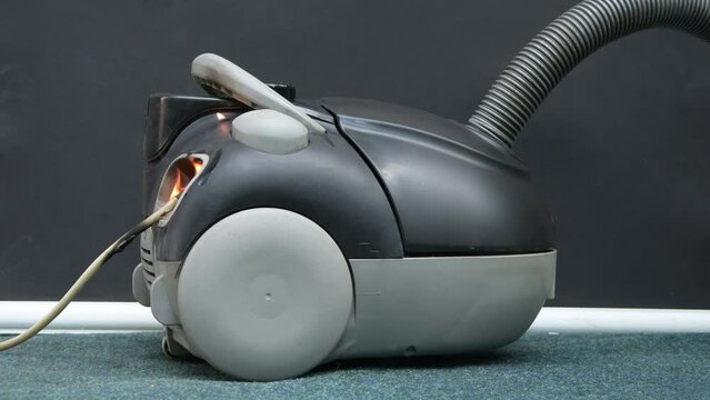 The vacuum cleaner is on fire in the apartment, the cause of the fire is a short circuit and an electrical fault. Smoke and fire, sparks fly, plastic melts.
