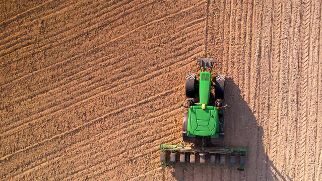 Aerial view of tractor with mounted seeder performing direct seeding of crops on plowed agricultural field. Farmer is using farming machinery for planting process, top view. High quality 4k footage