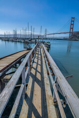 Fototapeta na wymiar Wooden pier with handrails heading to the boats against the Golden Gate Bridge in San Francisco, CA