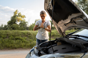 one mature woman stand by car with broken failed engine on the road