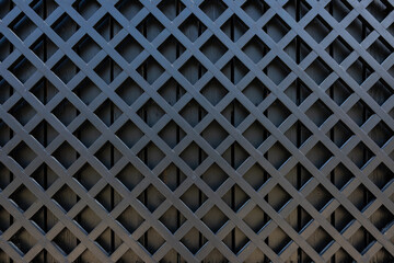 A fragment of a wooden fence made of painted black boards. Wooden diagonal lattice
