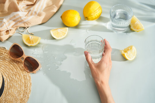 Hand with glass of water and lemons on summer table