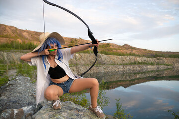 a beautiful girl in a blue wig and a straw hat with a bow and arrow in her hands.beautiful view of...