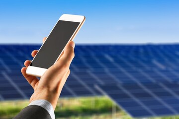 Hand of person showing smartphone with solar panels in the background.