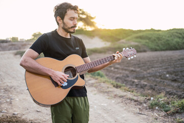 Portrait of young musician playing guitar on the road at sunset