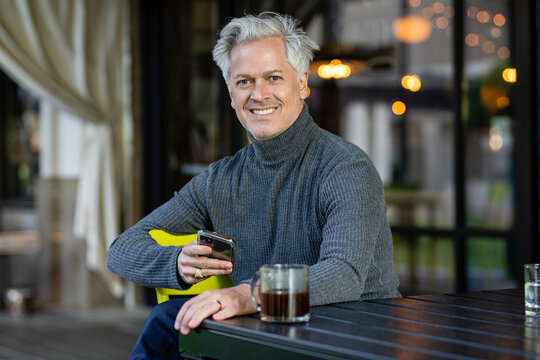 Happy Man Smiles At Camera With Cell Phone In Hand