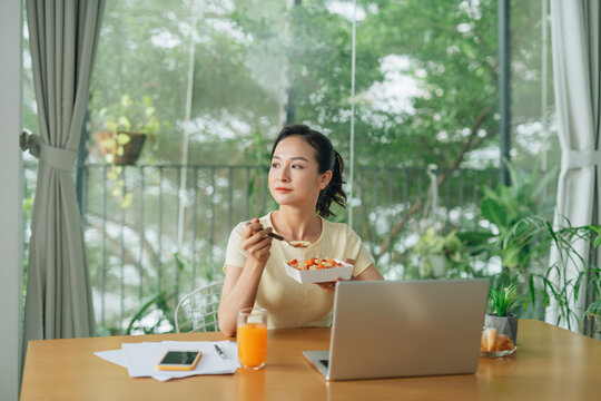 Smiling young asian woman having healthy lunch at office desk