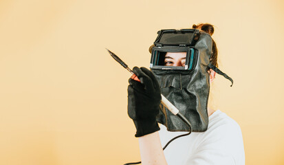 Young woman with a welder mask, gloves and welding tools smiling to camera with happy attitude.New...