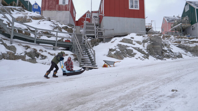 Arctic Greenland lifestyle: Inuk father pushes daughter's sled uphill